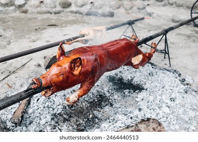 Closeup of the popular and delicious roasted pig known as "lechon baboy" skewered on a spit over burning charcoals on slow cooking or grilling. Selective focus. - Powered by Shutterstock