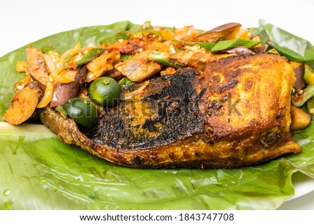 Close-up of popular grilled stingray fish with spices and vegetable served on banana leaf in Malaysia