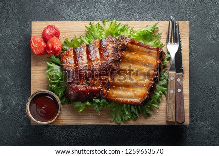 Closeup of pork ribs grilled with BBQ sauce and caramelized in honey on a bed of salad frisse. Tasty snack to beer on a wooden Board for filing on dark concrete background. Top view. Flat lay