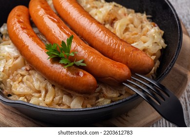 Close-up of pork sausages, or Wurstel, or wiener, or frankfurter on fried crauti or sauerkraut in a cast iron pan. 