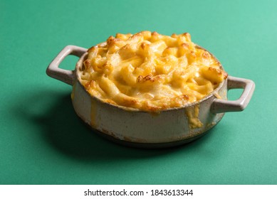 Close-up Of A Portion Of Mac And Cheese Baked In A Clay Plate. Home-baked Mac And Cheese Isolated On A Green Background.