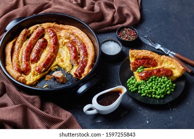 Close-up Of A Portion Of Toad In The Hole, Sausage Toad, Sausages In Yorkshire Pudding Batter On A Black Plate Served With Green Peas And Onion Gravy,  View From Above