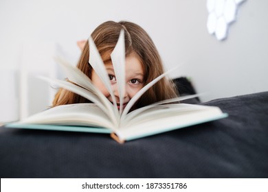 Close-up Portrait Of 6-year-old Girl, Shot Through Open Book. Real Life Moment