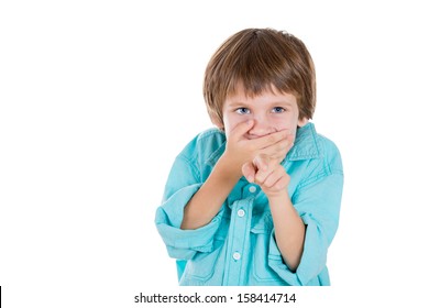 Closeup portrait of adorable young boy, pointing with one hand, closing mouth with other and laughing at you, isolated on white background with copy space