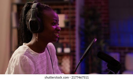 Closeup Portrait Of African American Online Radio Host Smiling And Talking While Broadcasting Live Sitting At Desk. Podcaster In Home Recording Studio With Boom Arm Microphone And Digital Audio Mixer.