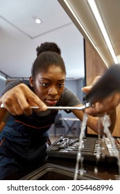 Closeup Portrait African Ethnicity Young Woman Plumber Unsuccessfully Trying To Fix Leaking Kitchen Tap. Selective Focus On Beautiful Work Woman's Face. Kitchen Tap With Water Stream.