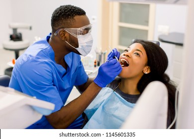 Close-up portrait of the african young woman patient examining by male dentist with tools in dental clinic. - Shutterstock ID 1145601335