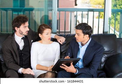 Closeup portrait of agent giving bad news to rich unhappy couple man woman sitting on black couch in house, apartment isolated on city urban background.  Financial budget troubles, adverse life events