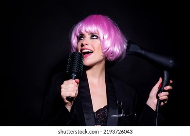 Close-up Portrait Of Amazing Female Model In Pink Wig With Comb And Hair Dryer. Studio Photo Funny Humoured Girl In Wigs.