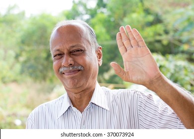 Closeup portrait, amiable old man waving hi or farewell, isolated outdoors background with green trees