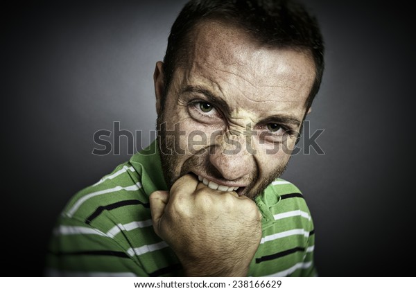 Closeup portrait of an angry guy biting his fist,\
looking at the camera.