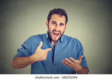 Closeup portrait of angry, mad, unhappy young guy pointing at himself asking you mean me, you talking to me, isolated on gray background. Negative human emotion facial expression feeling