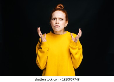 Close-up portrait of angry mad young woman in yellow sweater screaming on isolated black background, looking at camera . Pretty redhead lady model emotionally showing facial expressions, copy space.