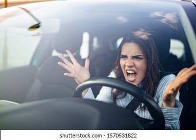 Closeup portrait, angry young sitting woman pissed off by drivers in front of her and gesturing with hands. Road rage traffic jam concept. Woman is driving her car very aggressive