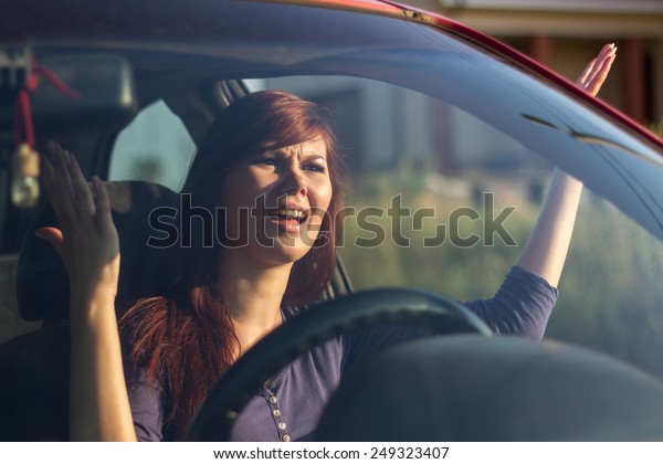 Closeup portrait, angry young sitting woman\
pissed off by drivers in front of her and gesturing with hands.\
Road rage traffic jam\
concept