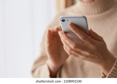 Closeup Portrait Of Anonymous Woman Wearing Beige Casual Style Sweater Holding Mobile Phone In Hands, Using Cell Phone For Online Communication, Typing Messages.