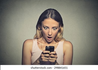 Closeup portrait anxious young girl looking at phone seeing bad news or photos with shocked disgusting emotion on her face isolated on gray wall background. Human reaction, expression