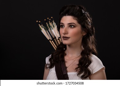Close-up portrait of a archer woman in white dress on black background. Greek goddess Artemis. Studio photo shoot. Professional makeup and hairstyle for a brunette with long dark hair. Young woman
