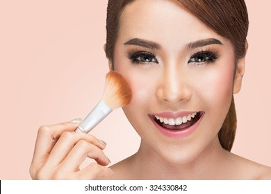 Closeup portrait of a asian woman applying dry cosmetic tonal foundation on the face using makeup brush, on pink background with clipping path.