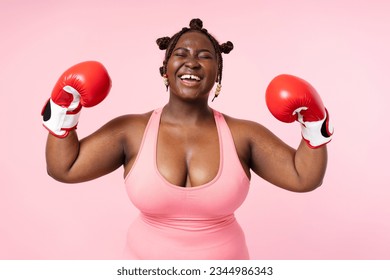 Closeup portrait of attractive body positive African American with closed eyes woman wearing red boxing gloves isolated on pink background. Plus size female training, fighting breast cancer concept - Powered by Shutterstock