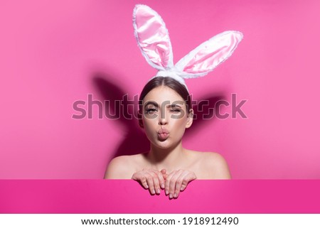 Close-up portrait of attractive cheerful girl wearing pink ears, air kiss. Easter bunny woman