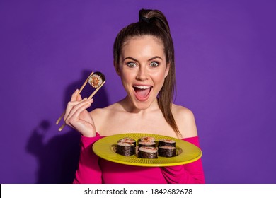 Close-up portrait of attractive hungry cheerful girl eating sushi with sticks isolated bright violet purple color background
