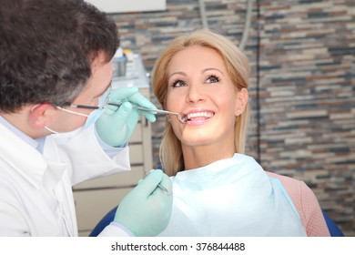 Close-up portrait of an attractive woman sitting at dentist office while male dentist checking her teeth. - Powered by Shutterstock