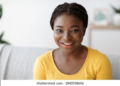 Closeup Portrait Of Attractive Young Black Woman Posing On Couch At Home, Beautiful African American Female With Braids Sitting On Sofa In Living Room, Looking And Smiling At Camera, Free Space