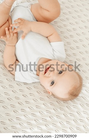 close-up portrait of a baby on a white cotton bed in a bright bedroom, a small smiling baby boy or girl upside down