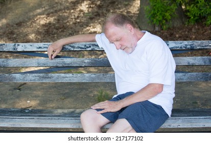 Closeup Portrait Bald Old Man In White Shirt, Blue Shorts, Exhausted, Resting On A Bench, Looking Down, Trying To Take A Power Nap, Isolated Outdoor Outside Background