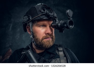 Close-up portrait of a bearded special forces soldier observes the surroundings in night vision goggles. Studio photo against a dark textured wall