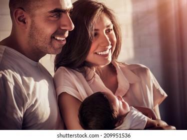Closeup portrait of beautiful arabic family at home in sunset light, happy parents holding on hands cute little daughter, happiness and love concept  