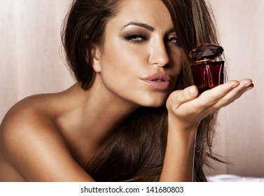 Close-up portrait of a beautiful brunette woman looking at camera, posing with her favorite perfume.
