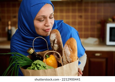 Close-up Portrait. Beautiful Charming Young Muslim Woman Of Middle Eastern Ethnicity, In A Blue Hijab, Posing With Paper Eco Shopping Bag Full Of Fresh And Healthy Organic Food. Shopping For Groceries