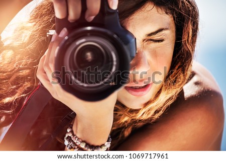 Closeup portrait of a beautiful girl with camera on the beach, cute young photographer taking picture, creative hobby, happy active summer vacation
