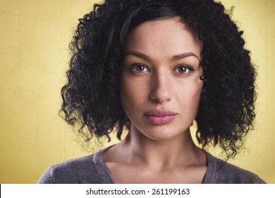 Closeup Portrait Of A Beautiful Latina Woman With Dark Skin Looking Serious, Isolated On Yellow Background.