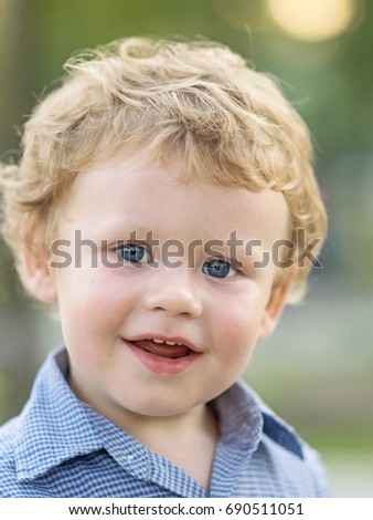 Close-up portrait of beautiful little boy smiling and looking to camera at summer day. Blurred background