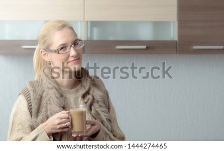 Close-up portrait of a beautiful mid age woman in glasses with cup of coffee. Attractive and happy blonde in sweater drinks latte. Copy space.