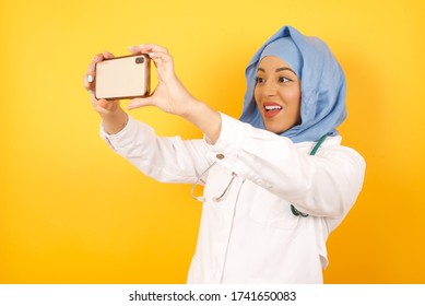 Close-up Portrait Beautiful Muslim Doctor Woman Wearing Medical Uniform And Hijab Taking A Selfie To Post It On Social Media Or Having A Video Call With Friends.