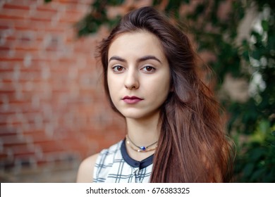 Closeup portrait of beautiful pensive young middle eastern Caucasian jewish woman with long dark hair, black brown eyes, looking in camera. Girl in white plaid shirt against brick wall. Natural beauty