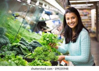 Closeup portrait, beautiful, pretty young woman in sweater picking up, choosing green leafy vegetables in grocery store