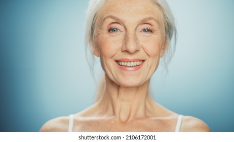 Close-up Portrait Of Beautiful Senior Woman Looking At Camera And Smiling Wonderfully. Gorgeous Elderly Lady With Natural Lush Grey Hair, Blue Eyes. Beauty And Dignity Of Old Age