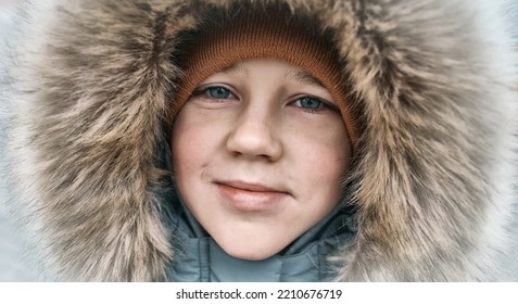 Close-up Portrait Of Beautiful Smiling White Boy In A Hood On A Winter Snowy Day. Happy Child Dressed In Warm Clothing, Snow, Holiday Concept.