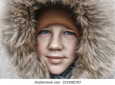 Close-up Portrait Of Beautiful Smiling White Boy In A Hood On A Winter Snowy Day. Happy Child Dressed In Warm Clothing, Snow, Holiday Concept.