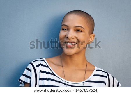 Closeup portrait of beautiful stylish woman on lightblue background. Smiling bald girl looking at camera with copy space. Cheerful and satisfied young woman with shaved head.