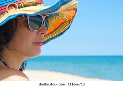 Closeup portrait of a beautiful woman wearing sunglasses and a colourful straw sunhat at the seaside for protection from the sun - Powered by Shutterstock