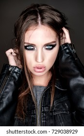 Close-up portrait of beautiful young  brown-haired woman with big sensual lips and languishing look with smoky eyes make-up in jeans denim and leather jacket on dark background