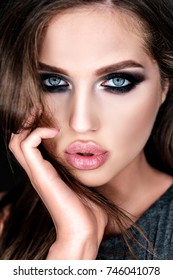 Close-up portrait of beautiful young brown-haired woman with big sensual lips, blue eyes and languishing look on dark background. Gorgeous glamour lady portrait