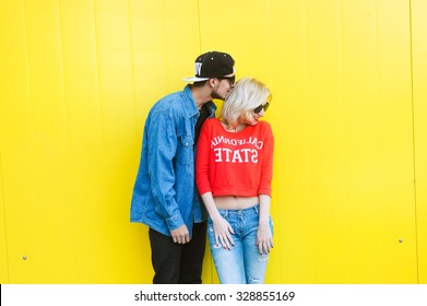 close-up portrait of a beautiful young couple in love bright blonde girl with red lips and a guy with a beard wearing a cap hipsters  yellow background smiling and posing lifestyle  telephone selfie