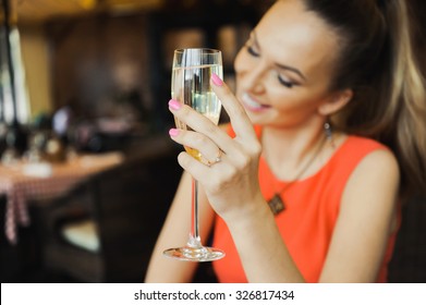 Close-up Portrait Of A Beautiful Young Elegant Sexy Blonde Woman In The Cafe With A Glass Of Champagne,White Wine  Smiling  And Drink Posing, With A Ring On Her Finger, She Is Engaged